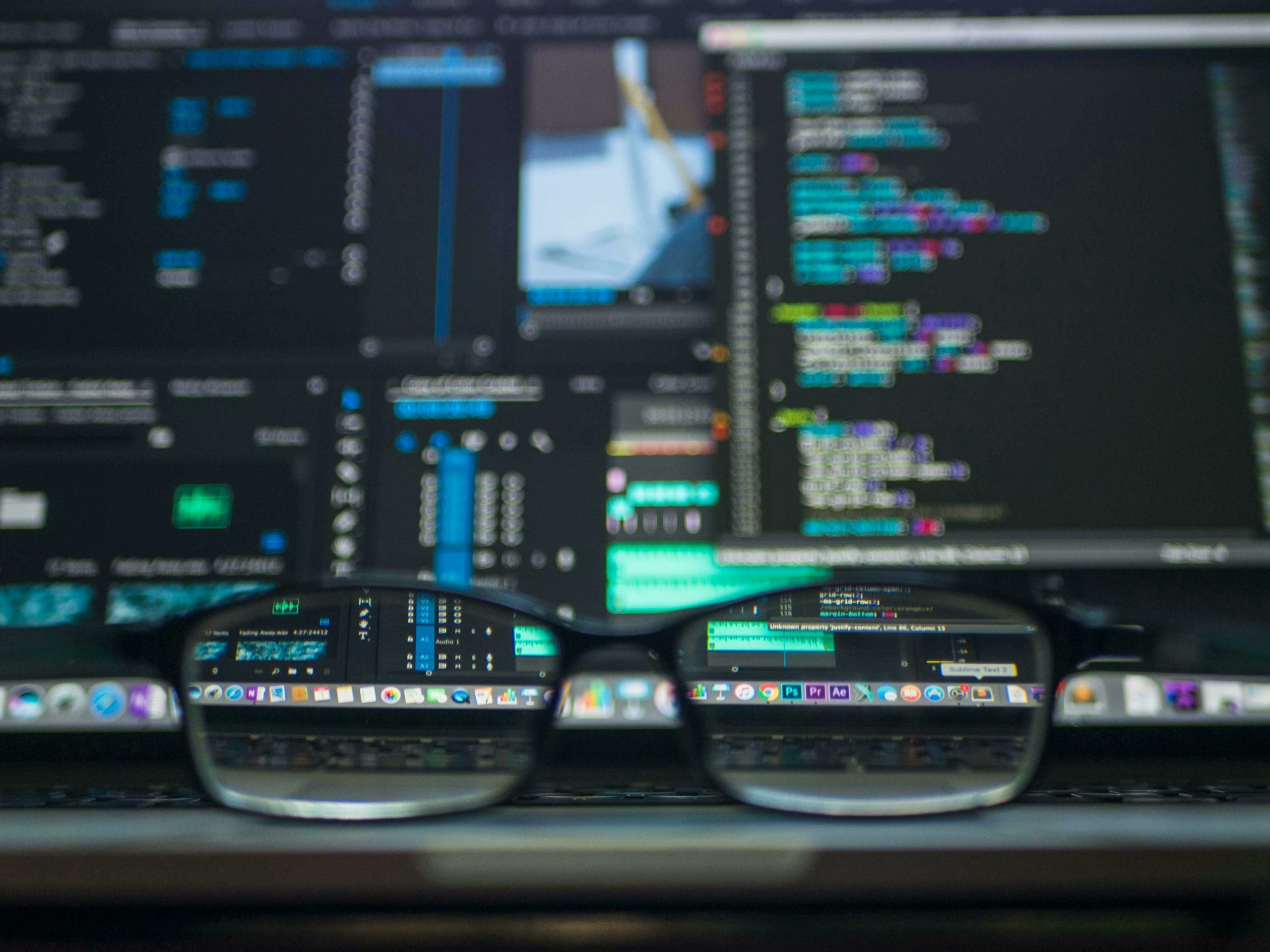 A pair of glasses in front of computer screens